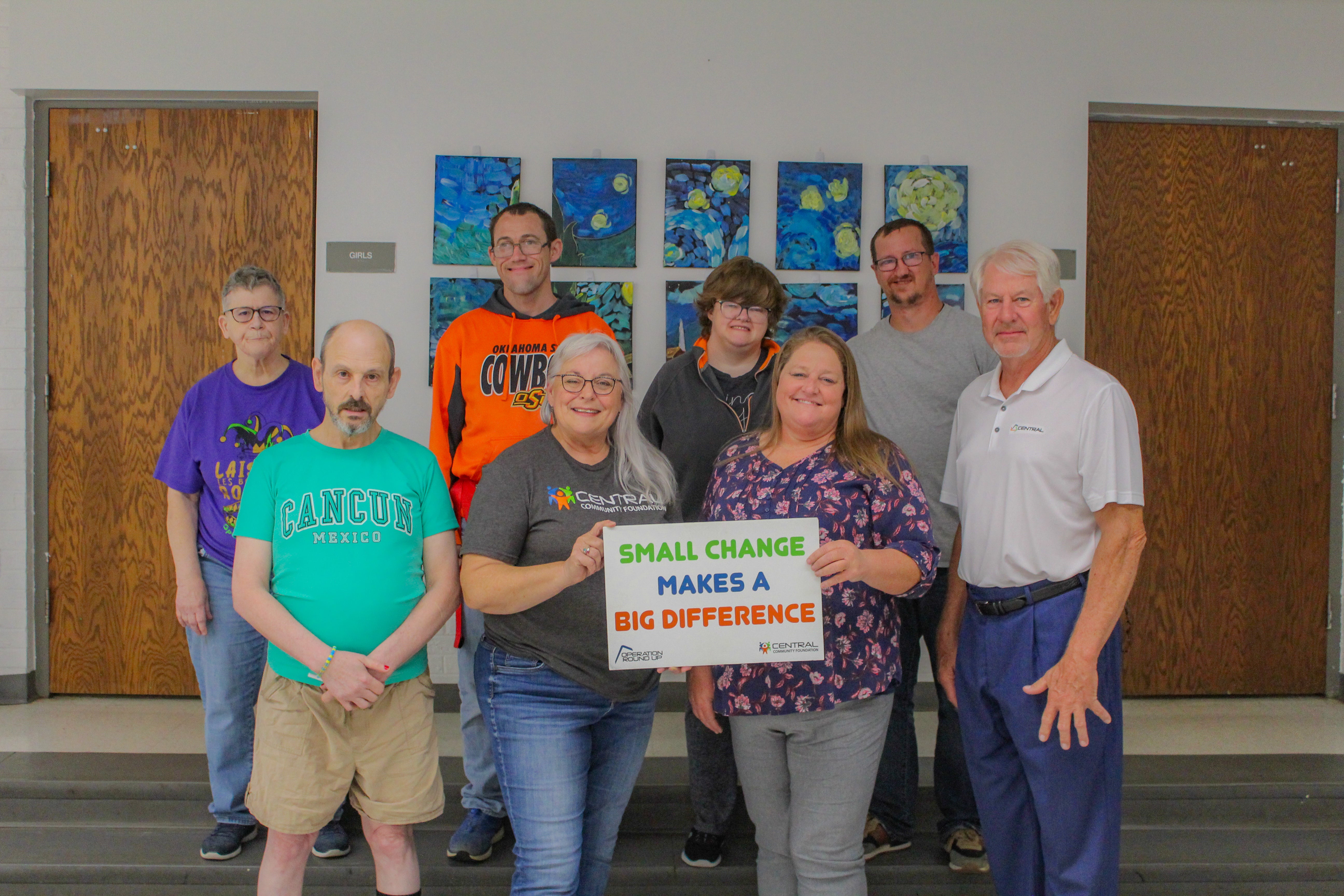 From left to right: (back row) Mpower clients Vicki, Jeffrey, Emily and Activity Director Jerry McDoughall. (Front row) Mpower Client Danny, Central Community Foundation board member Donna Dollins, MPower Executive Director Amy Spiva, and Central Trustee Ken Starks. The group stands in front of artwork made by MPower clients from art classes sponsored by the Central Community Foundation grant.
